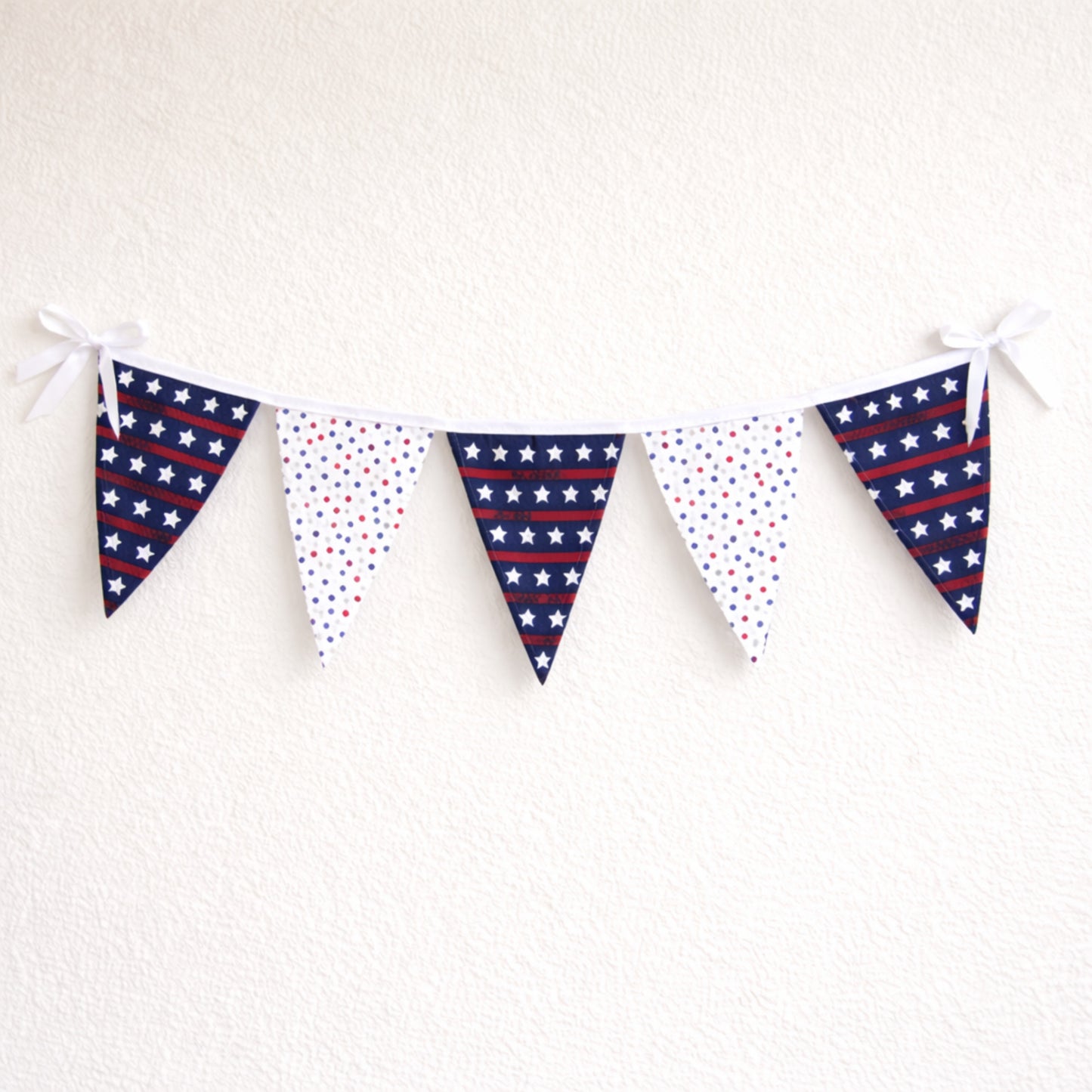 Large patriotic fabric bunting banner with red white and blue star flags and white binding hanging on a neutral wall
