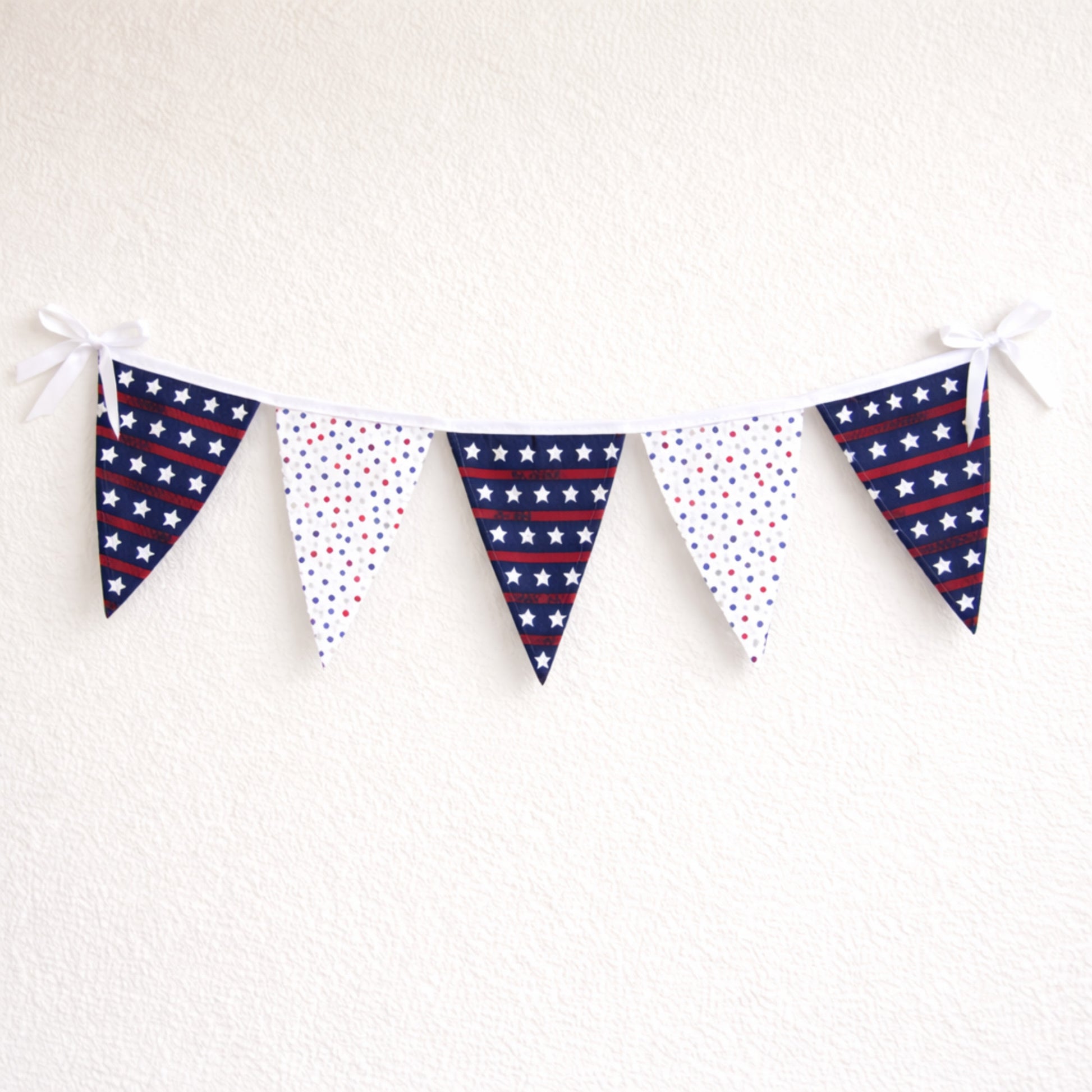 Large patriotic fabric bunting banner with red white and blue star flags and white binding hanging on a neutral wall
