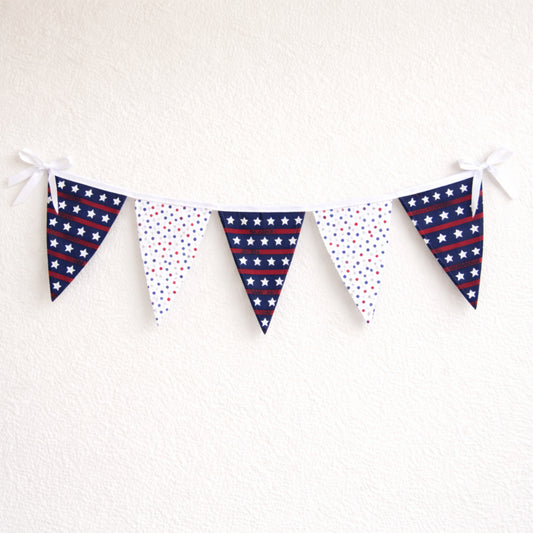 Large patriotic fabric bunting banner with red white and blue star flags and white binding hanging on a neutral wall
