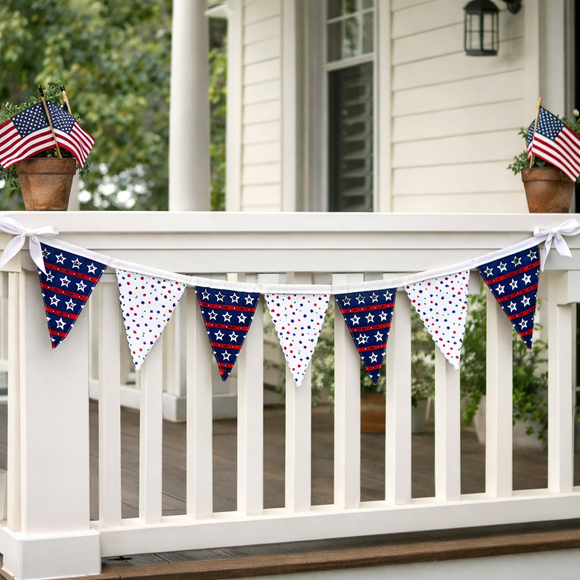 Handmade patriotic fabric bunting banner with seven red white and blue star flags displayed on a white porch railing for Fourth of July decor