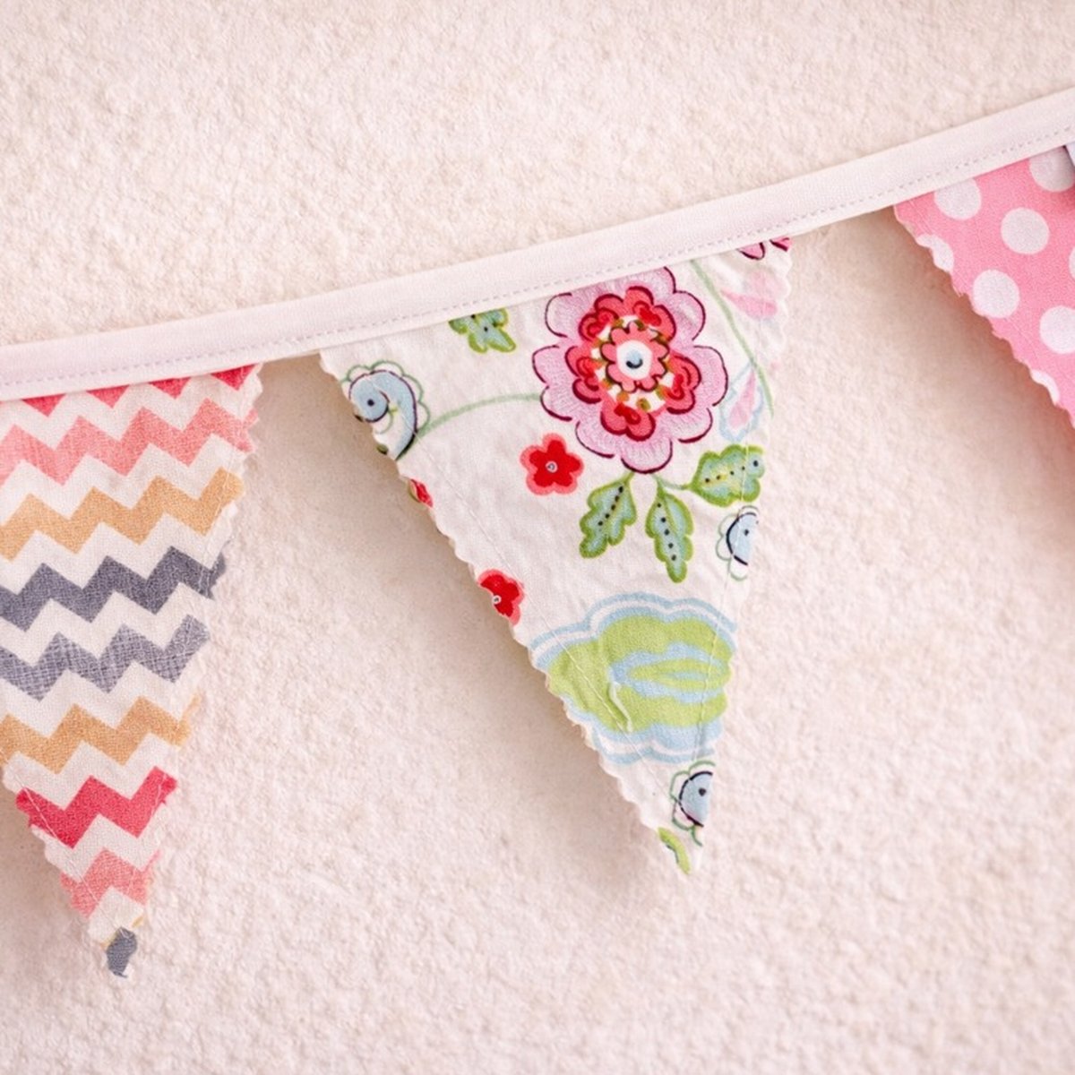 Colorful fabric bunting with floral and zigzag patterns on a light pink background