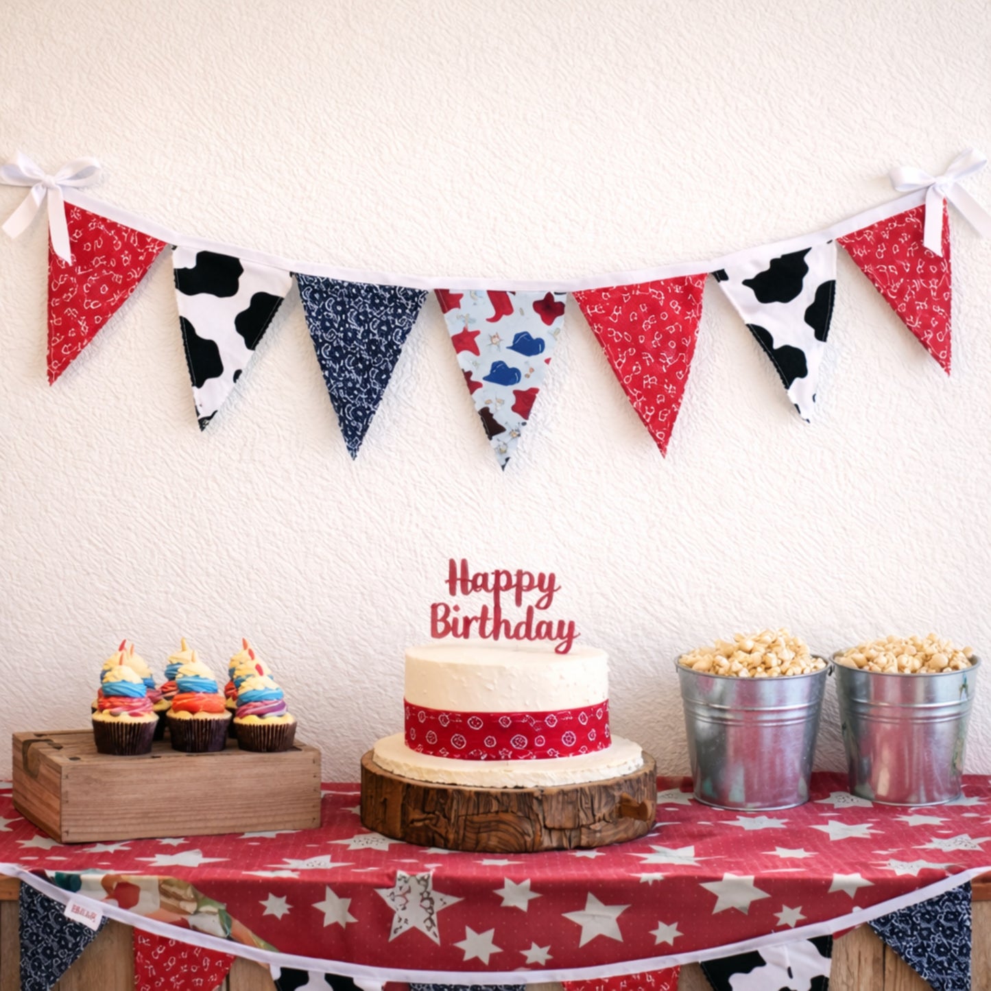 Western cowboy themed birthday party table with fabric bunting banner above cake and cupcakes