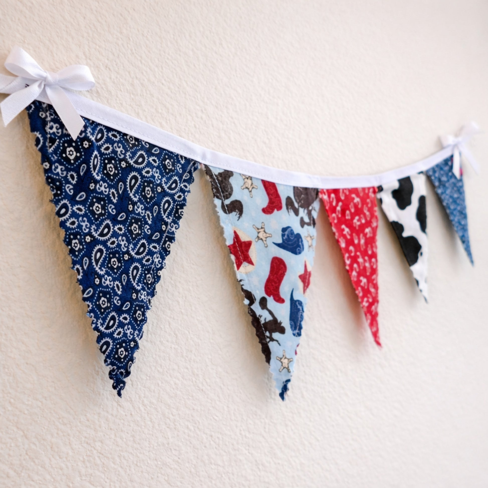 Angled view of western cowboy themed fabric bunting banner with red bandana cow print and paisley fabric flags