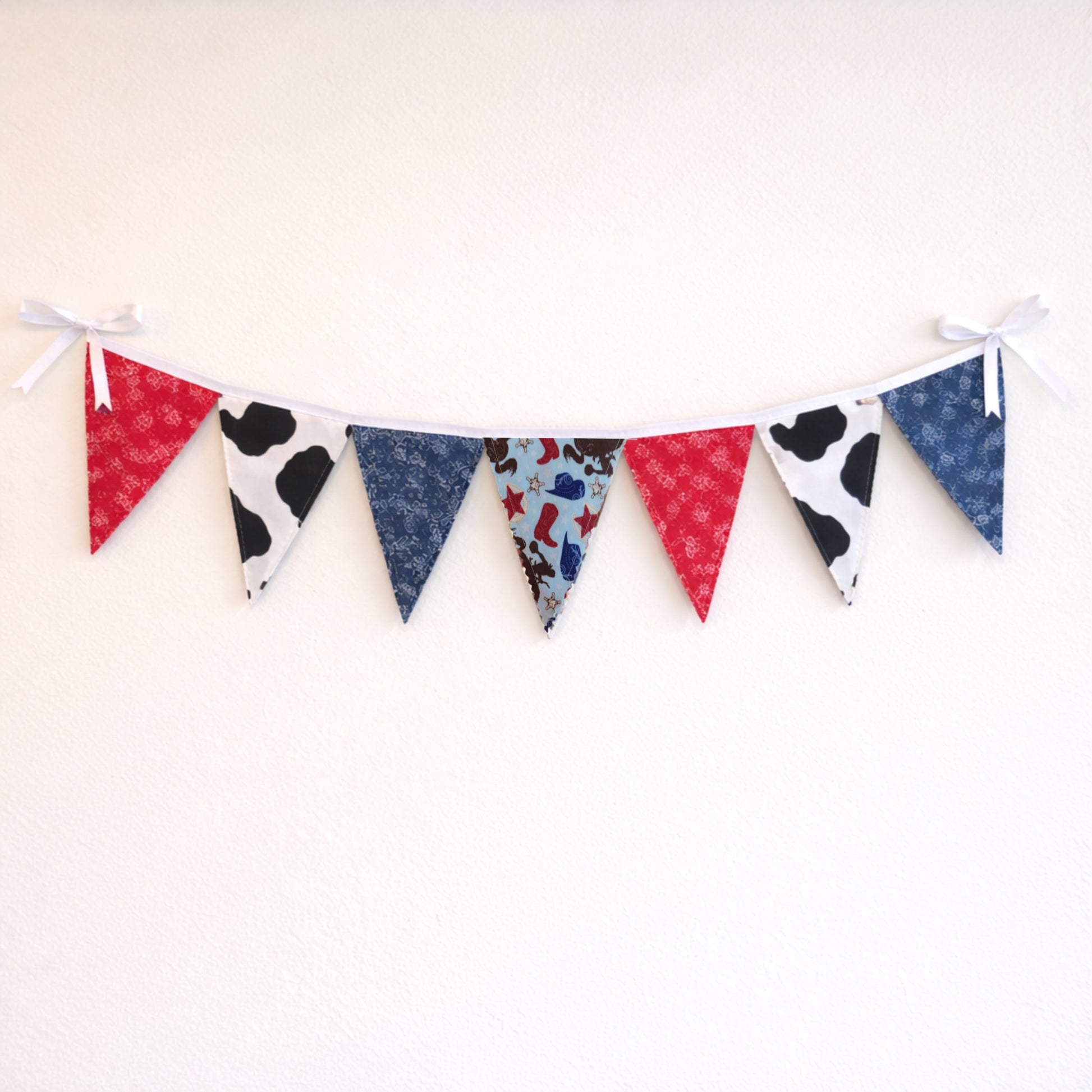 Western cowboy themed fabric bunting banner with red bandana, cow print and blue paisley flags hanging on a neutral wall