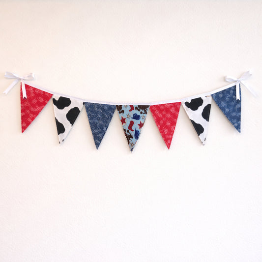 Western cowboy themed fabric bunting banner with red bandana, cow print and blue paisley flags hanging on a neutral wall