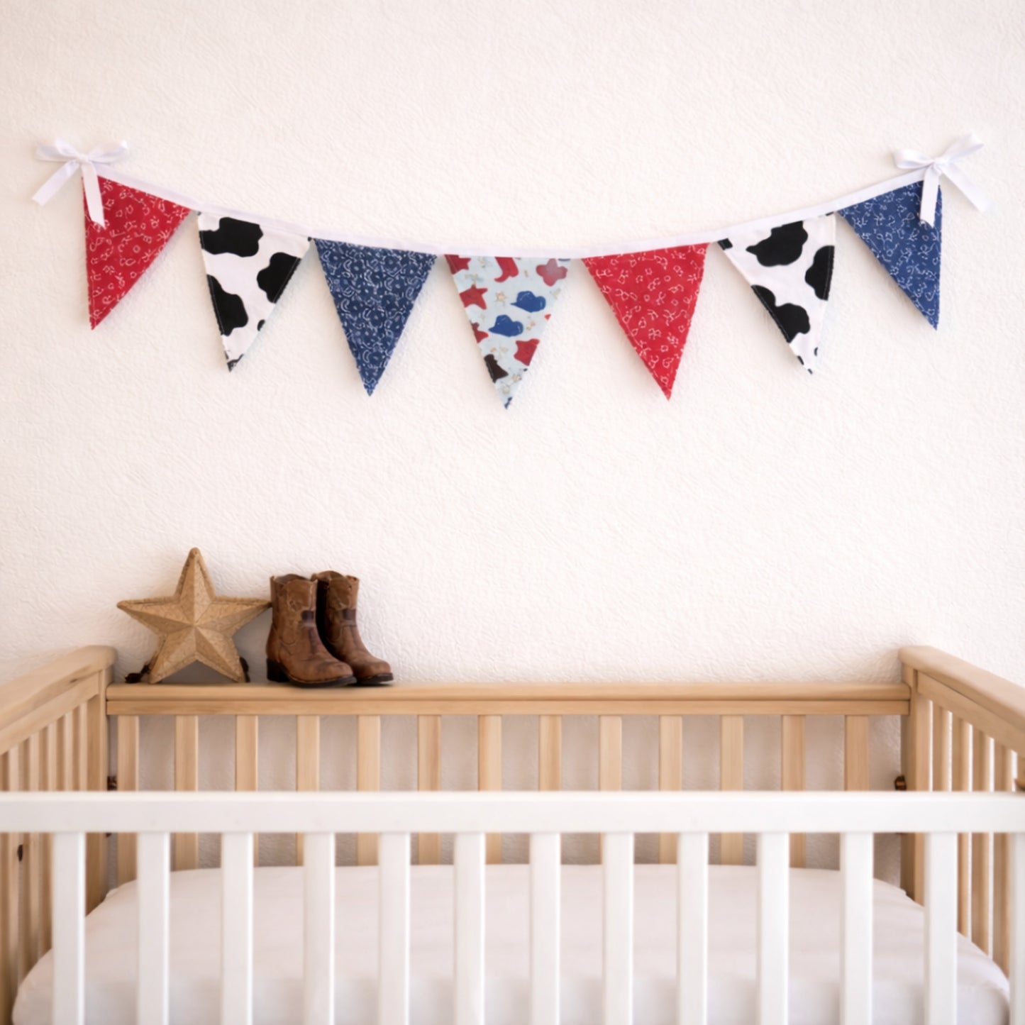 Western themed fabric bunting banner hanging above baby crib with cowboy boots nursery decor
