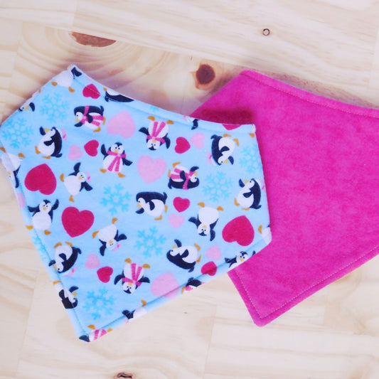 Set of two bandana bibs. Dancing penguins with red and pink hearts on a light blue fabric and solid hot pink bibs